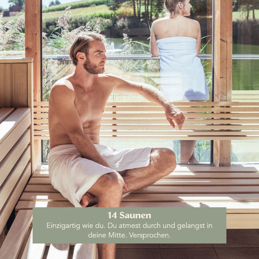 Ein Mann sitzt auf einer Bank in einer Sauna, ohne Hemd, mit einem Handtuch um die Taille. Eine Frau steht hinter ihm, ebenfalls in einem Handtuch, und schaut aus dem Glasfenster.