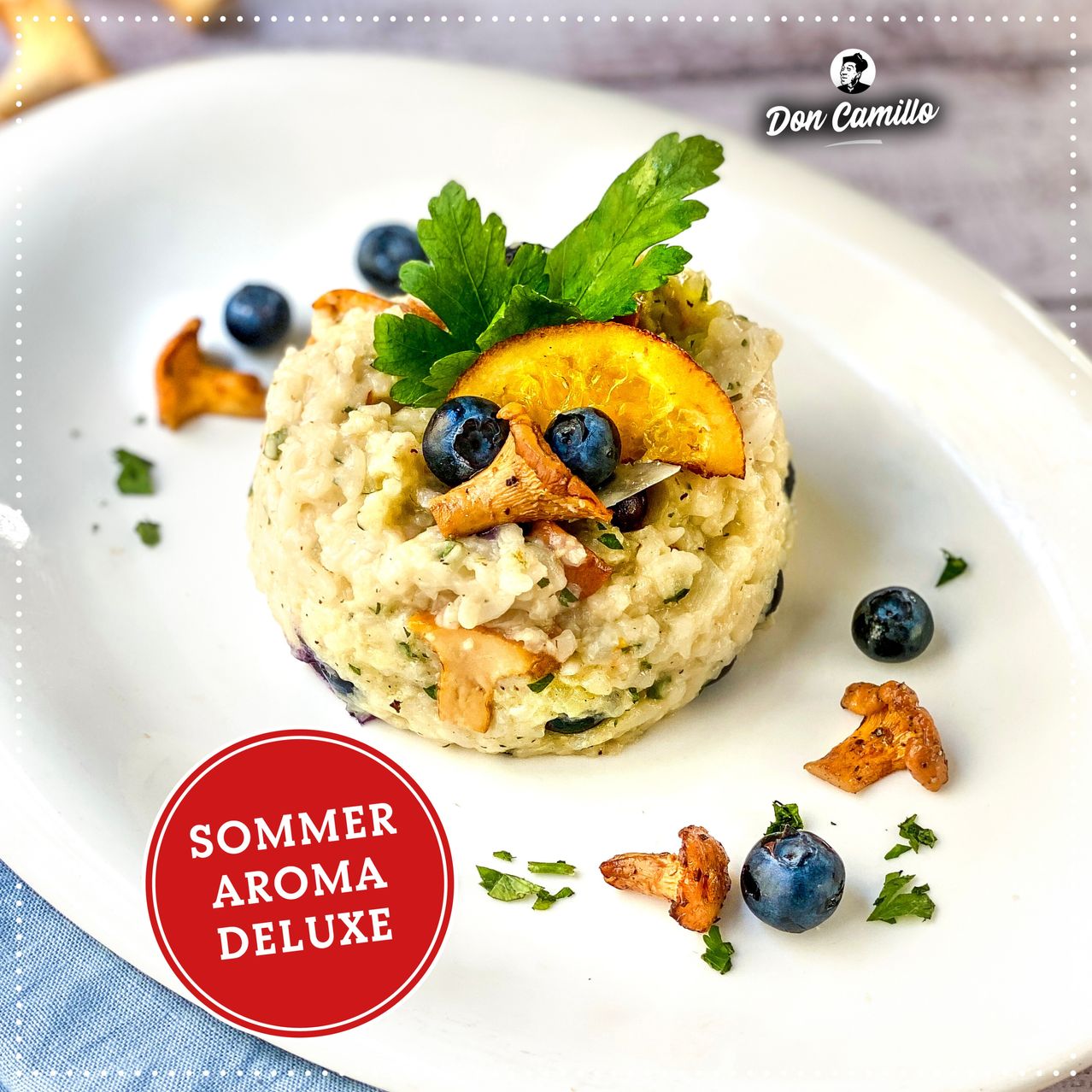 Ein Teller mit einem cremigen Gericht, das mit Blaubeeren, einer Orangenscheibe und Pilzen garniert ist. Dekoriert mit Petersilienblättern und einem roten Etikett mit der Aufschrift 'Sommer Aroma Deluxe.'