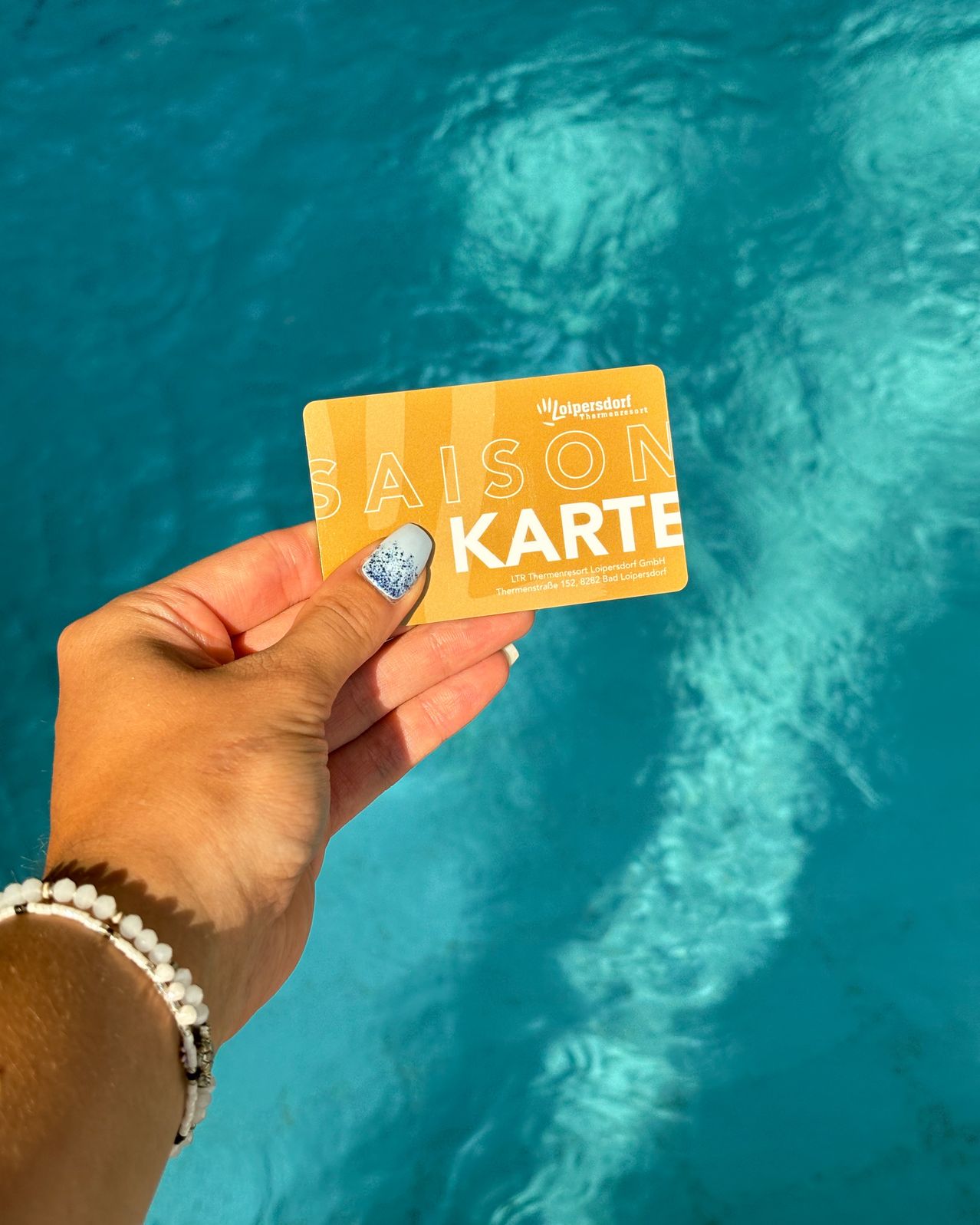 A hand holding a yellow card with the text 'SAISON KARTE' against a blue water background.