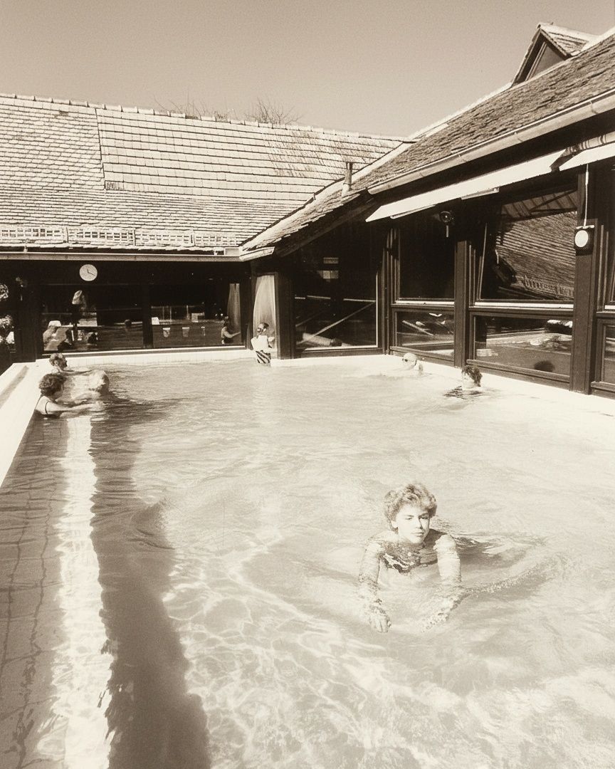 Ein Schwarz-Weiß-Foto von Menschen, die in einem Pool schwimmen, mit einem Gebäude im Hintergrund.