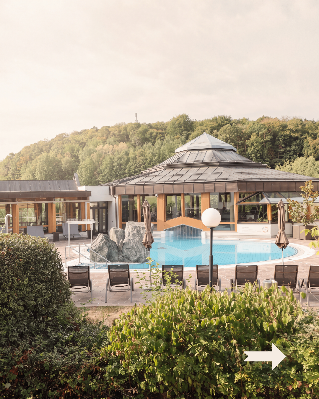 A modern resort with a large pool surrounded by rocks and lounge chairs under a gazebo with a metal roof.