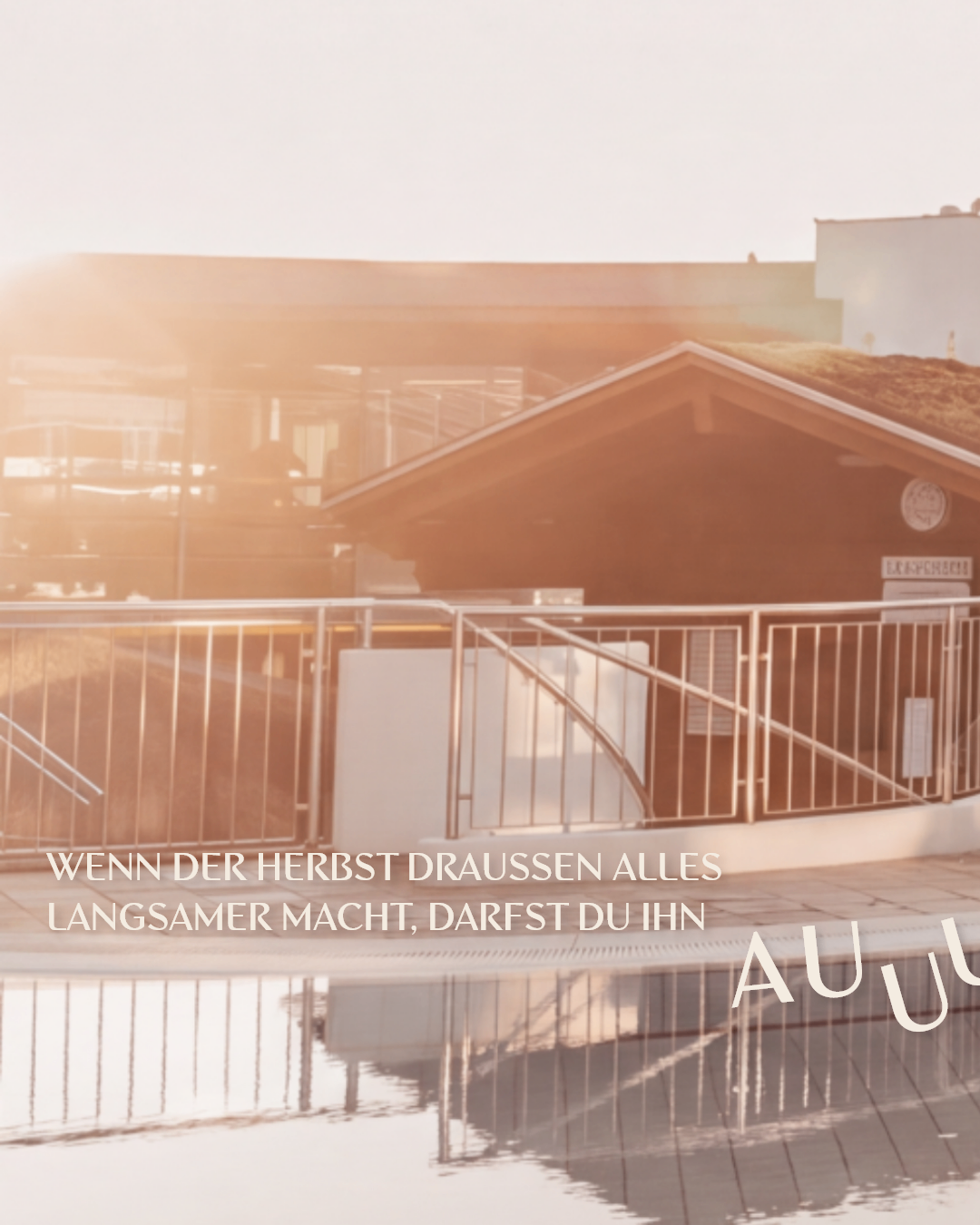 A building with a sod roof and a metal fence in front of a pool with text in German.
