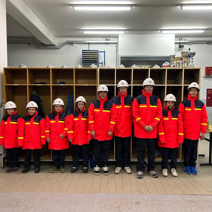 Gruppe von Kindern in roten Uniformen und weißen Helmen steht vor einer Reihe von Holzschränken.