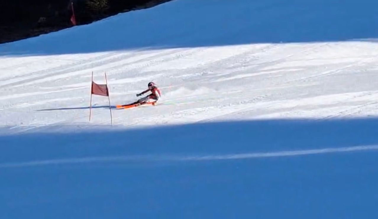 A skier is descending a snowy slope, passing by a red flag marker. They are wearing a helmet and ski gear.