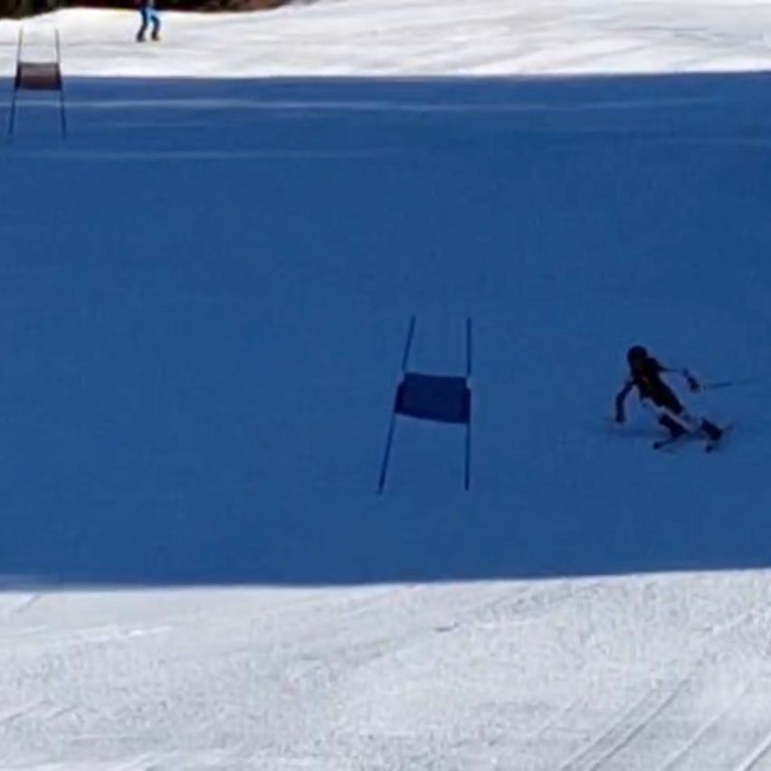 A skier navigates through a slalom course, passing between blue flags on a snowy slope.