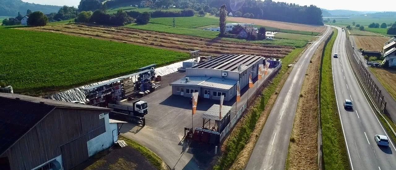 Luftaufnahme eines Bauernhofs mit Feldern, Gebäuden und einer Straße. Ein LKW ist in der Nähe der Gebäude geparkt.