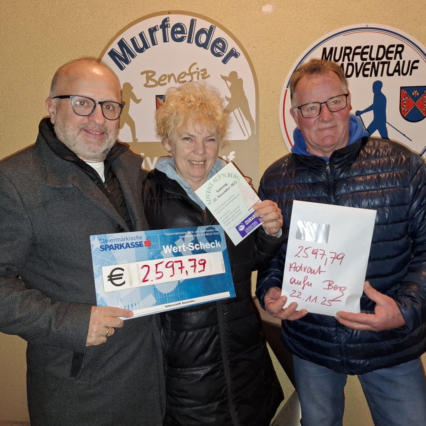 Drei Menschen stehen eng zusammen und lächeln für ein Foto. Der Mann auf der linken Seite hält einen Bankbeleg über 2597,79 Euro. Die Frau in der Mitte hält ein Zertifikat und ein Stück Papier. Der Mann auf der rechten Seite hält ein Blatt mit 2597,79 Euro darauf. Sie stehen vor einem Schild mit 'Murfelder Adventlauf'.