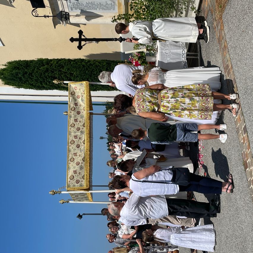 A group of people are gathered outside a building. They are standing in a line and appear to be attending a ceremony. A banner is held up in front of them.