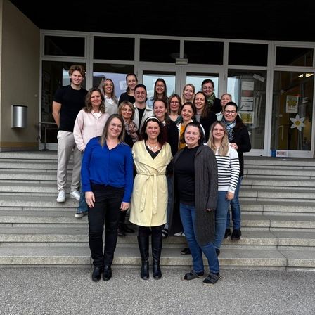 Eine Gruppe von Menschen, sowohl Männer als auch Frauen, stehen auf den Stufen eines Gebäudes und lächeln für ein Foto.