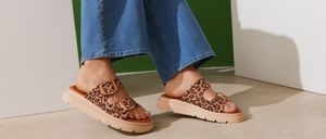 Eine Person in blauen Jeans und Leopardenmuster-Sandalen mit Schnallen und dicker Sohle.