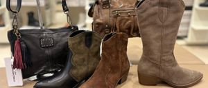 Eine Auswahl an braunen und schwarzen Wildleder- und Lederstiefeln mit verschiedenen Designs und Verzierungen, die auf einer beigefarbenen Oberfläche ausgestellt sind.