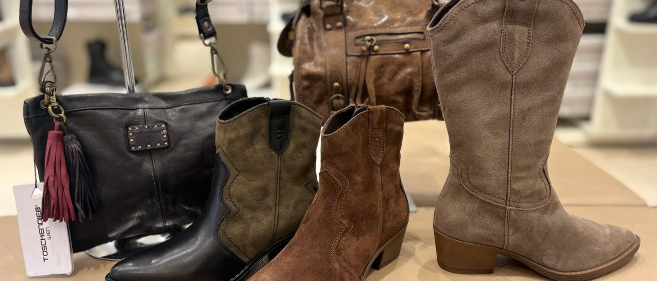 Eine Auswahl an braunen und schwarzen Wildleder- und Lederstiefeln mit verschiedenen Designs und Verzierungen, die auf einer beigefarbenen Oberfläche ausgestellt sind.