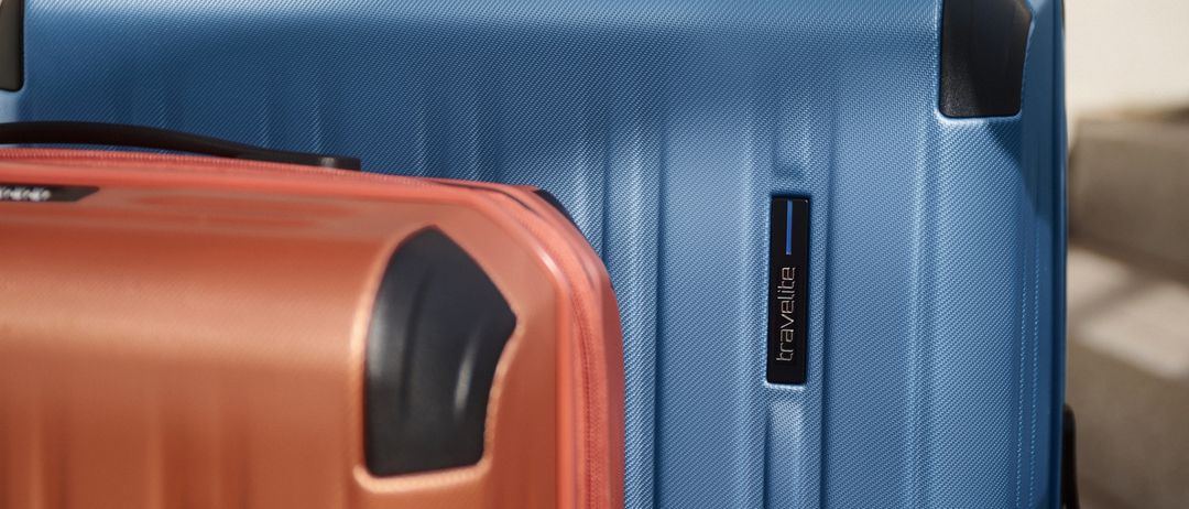 Zwei Koffer, einer blau und einer orange, stehen nebeneinander auf einer hellen Oberfläche, möglicherweise einer Treppe.