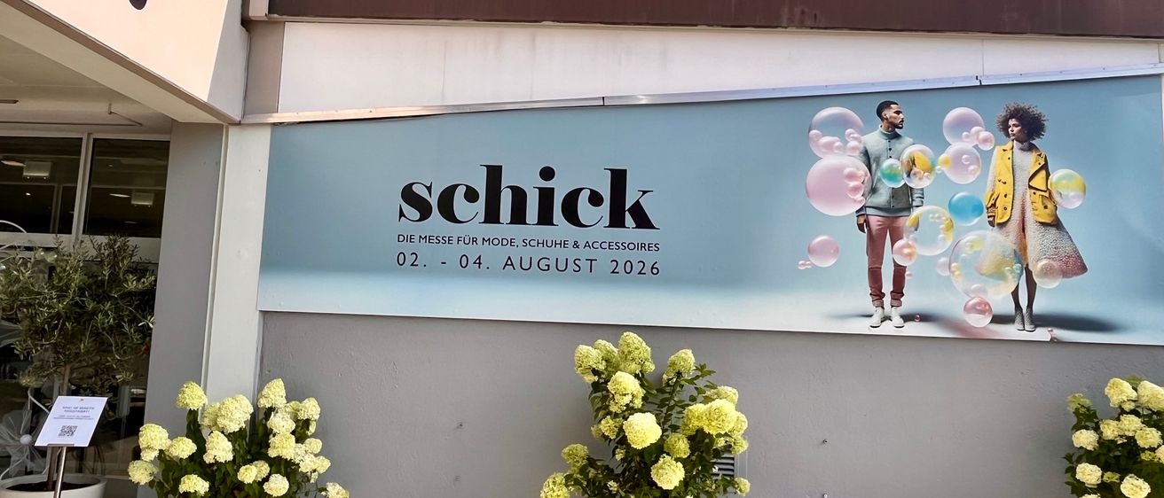 Ein Werbebanner für die Schick Modemesse mit zwei Personen im Hintergrund und zwei Topfpflanzen im Vordergrund.