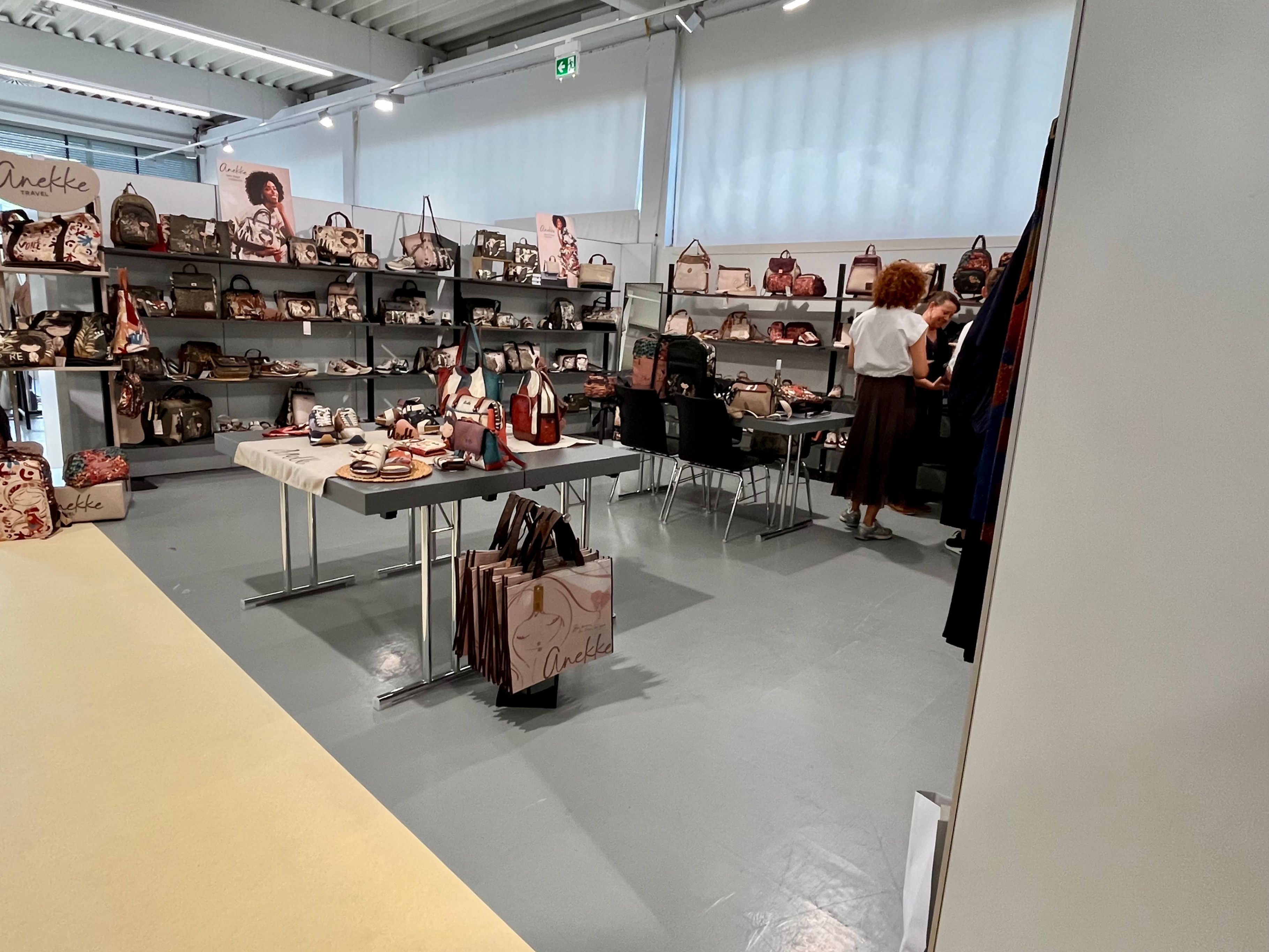 Ein Handtaschenladen mit Regalen voller Taschen und einer Frau, die neben einem Tisch mit Taschen steht.