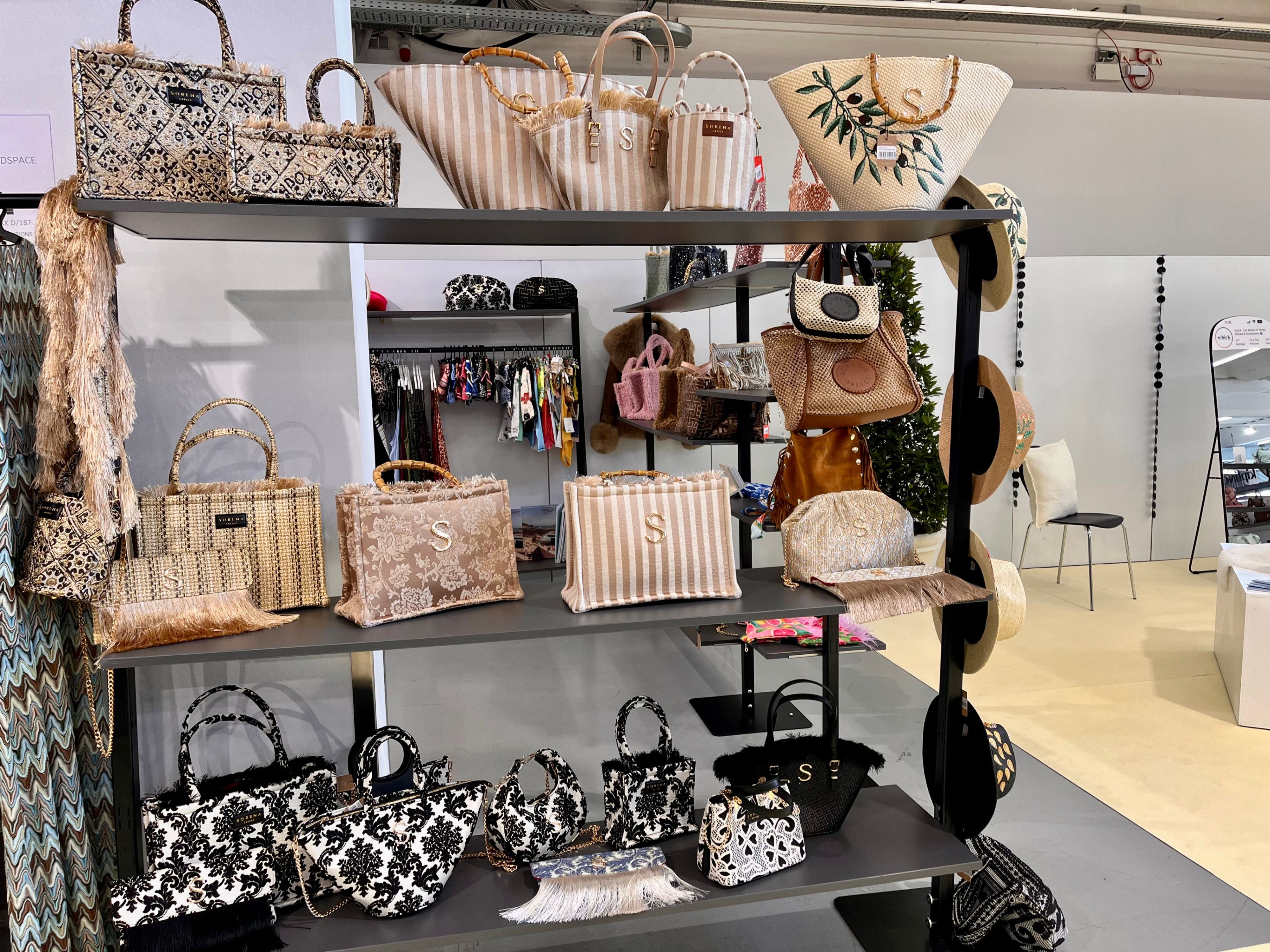 Ein Geschäft mit verschiedenen Handtaschen zur Schau, darunter gestreifte, florale und schwarz-weiße Designs. Die Regale sind mit Taschen gefüllt, und einige hängen an Haken.