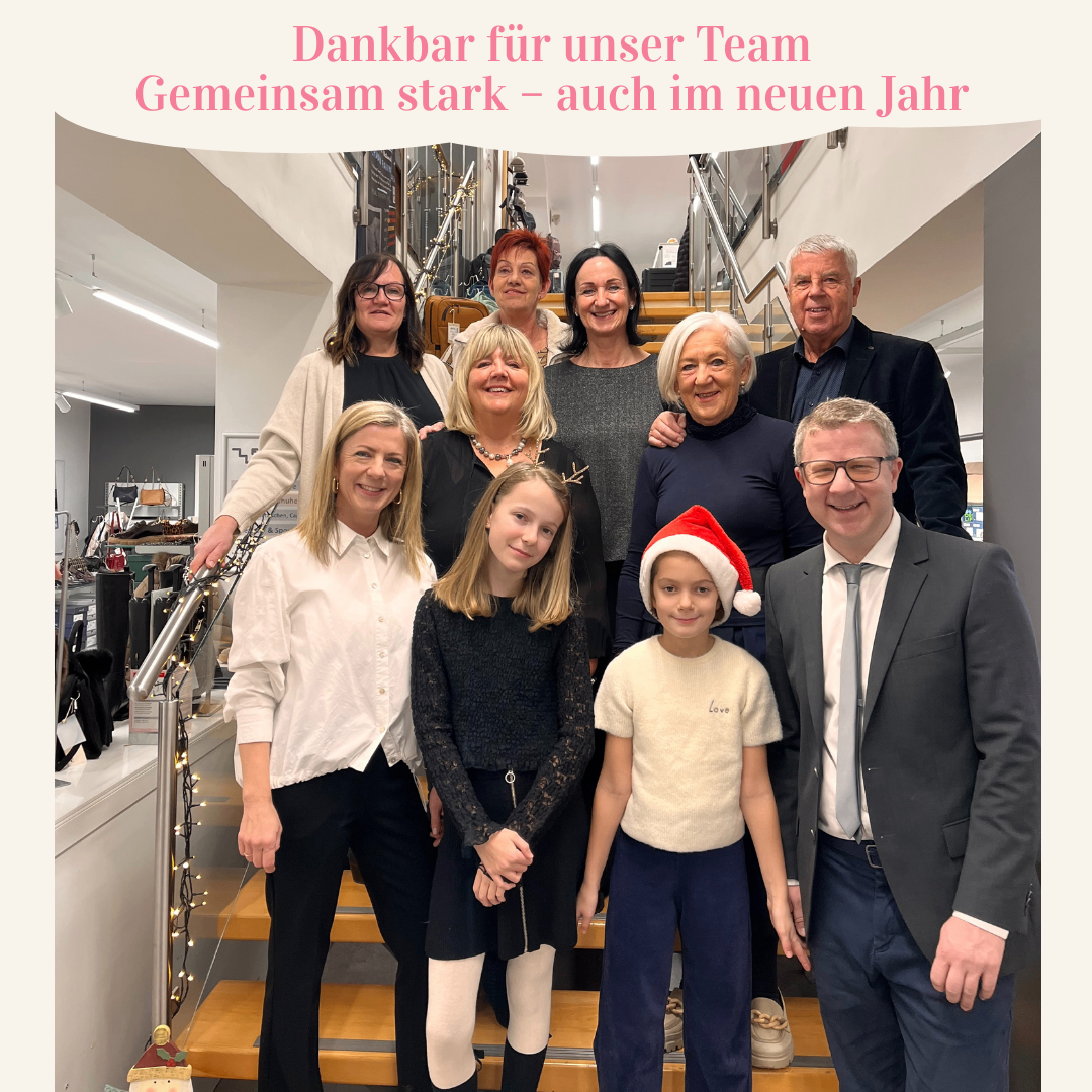 Eine Gruppe von Erwachsenen und Kindern steht gemeinsam auf einer Treppe und lächelt für ein Foto. Sie tragen Feiertagskleidung, einschließlich Weihnachtsmützen. Das Bild hat eine festliche Überlagerung mit dem Text: 'Dankbar für unser Team. Gemeinsam stark - auch im neuen Jahr.'