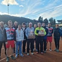 Eine Gruppe von Tennisspielern steht auf einem Tennisplatz, einer hält einen Pokal. Sie tragen Medaillen und Turnschuhe.