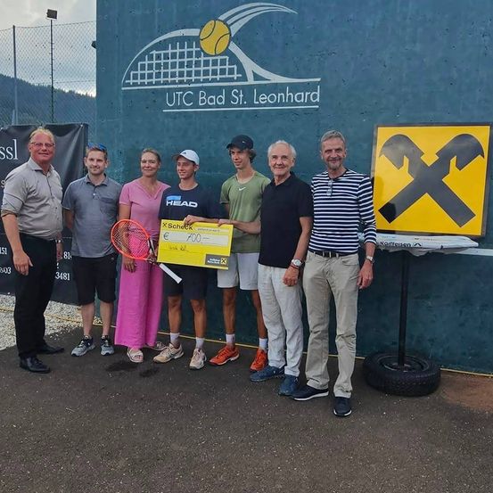 Eine Gruppe von Menschen posiert für ein Foto auf dem Tennisplatz des UTC Bad St. Leonhard. Sie halten eine Tennisschläger und einen Scheck.