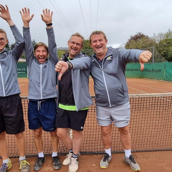 Vier Männer stehen auf einem Tennisplatz und posieren für ein Foto mit erhobenen Händen. Sie alle haben breite Lächeln auf ihren Gesichtern.