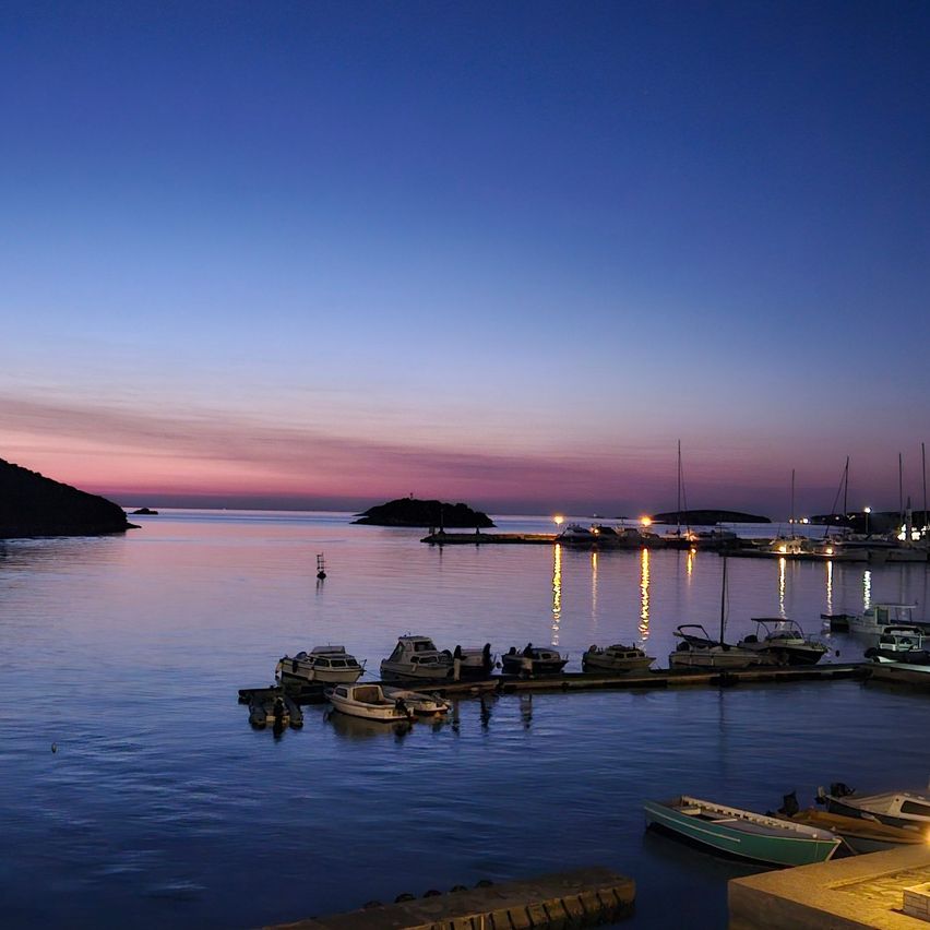 Ein friedlicher Hafen in der Dämmerung mit angedockten Booten und einer ruhigen See unter einem farbenfrohen Himmel.