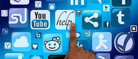 Ein Bild einer Hand, die auf verschiedene Social-Media-Symbole auf blauem Hintergrund zeigt. Symbole umfassen Facebook, YouTube, Twitter und mehr.