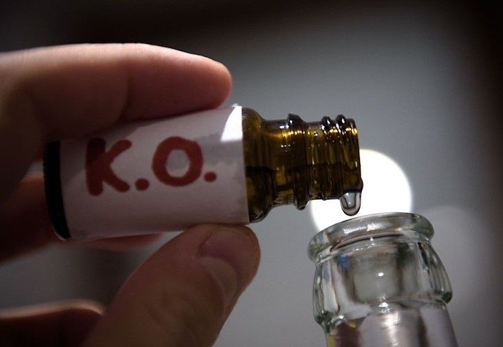 Eine Hand hält eine Flasche mit einem Tropfer, beschriftet mit K.O., die Flüssigkeit in eine Glasflasche gibt.