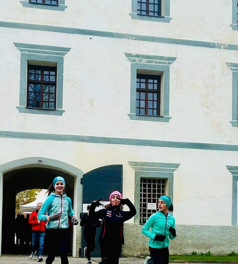 Drei Frauen laufen vor einem weißen Gebäude mit Bogenfenstern. Zwei von ihnen tragen Mützen und eine hat eine rosa Bandana.