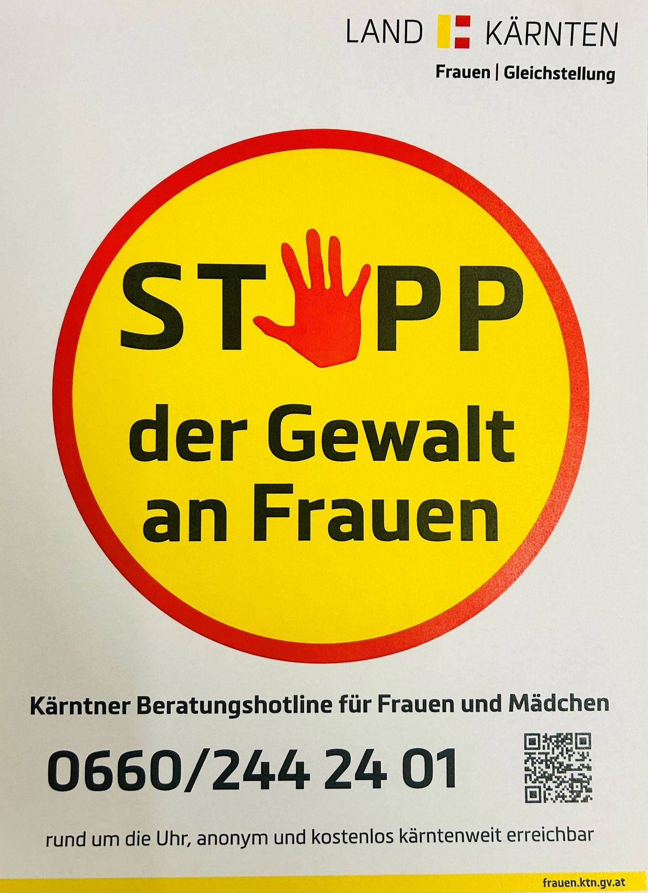Ein gelber runder Schild mit einer roten Hand und den Worten STOPP der Gewalt an Frauen. Darunter steht eine Telefonnummer mit einem QR-Code auf der rechten Seite.