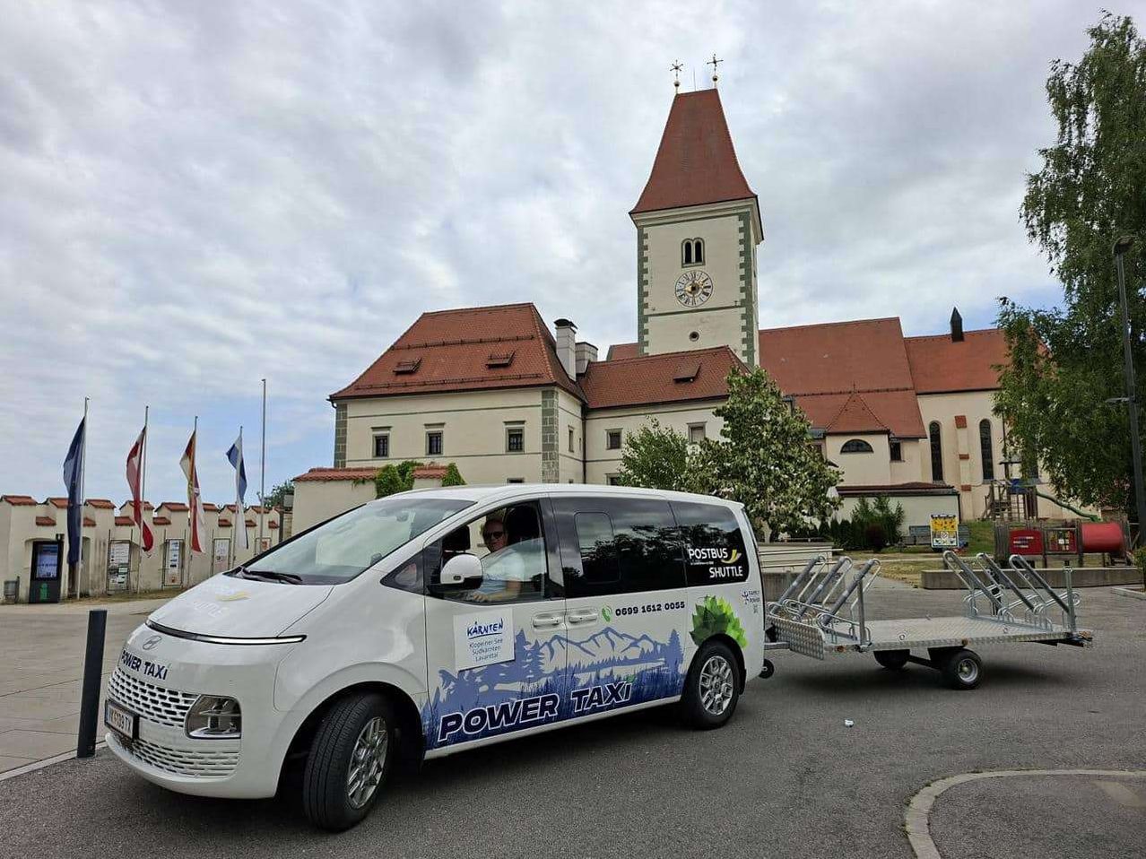 A white electric vehicle, branded 'Power Taxi', is parked in front of a historic building with a clock tower.