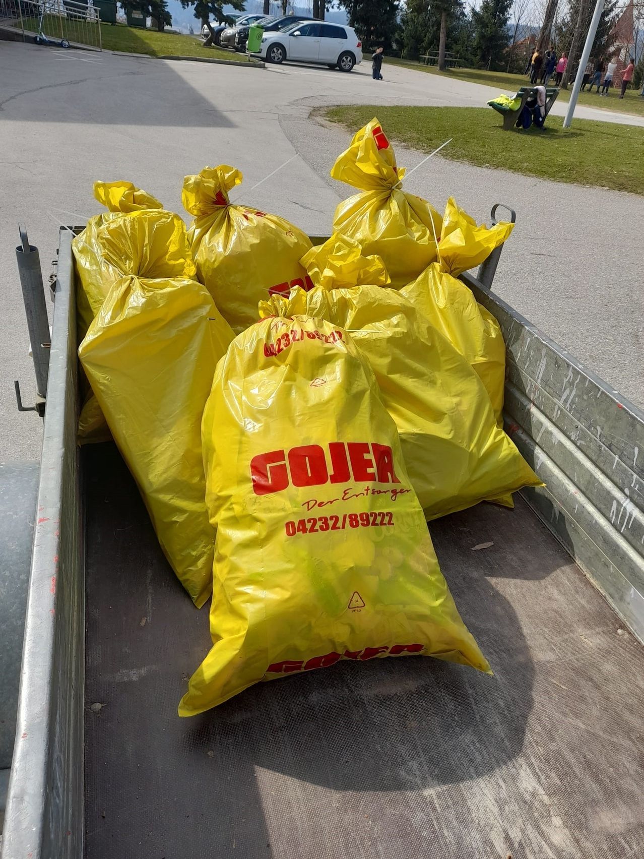 Ein Laderaum mit mehreren gelben Sojer-Säcken, einschließlich einer Kontaktnummer und einem Warnsymbol, auf einer Straße mit einem Grasbereich und einem Pfosten im Hintergrund.