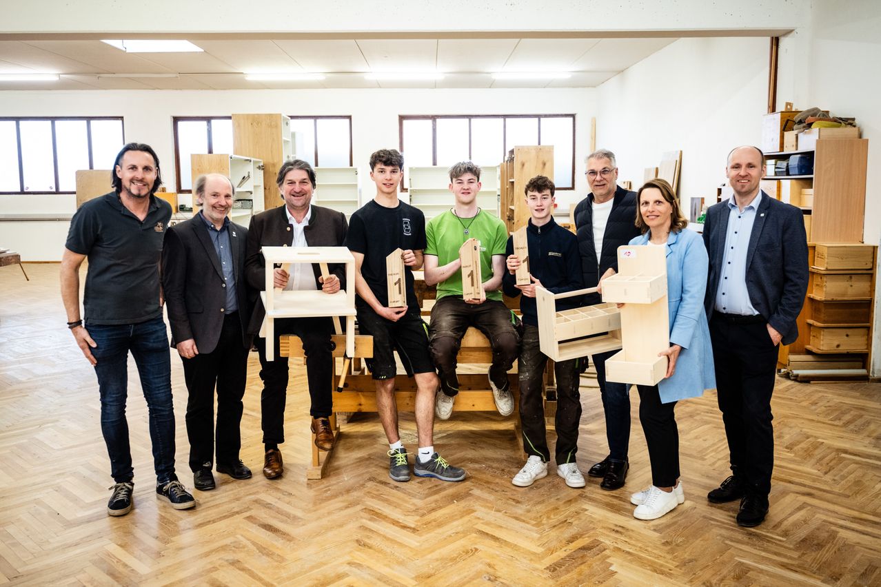 Eine Gruppe von Personen, wahrscheinlich in einer Werkstatt, posiert für ein Foto mit Holzgegenständen in der Hand. Sie sind lässig gekleidet und scheinen an einem Holzbearbeitungsprojekt beteiligt zu sein.