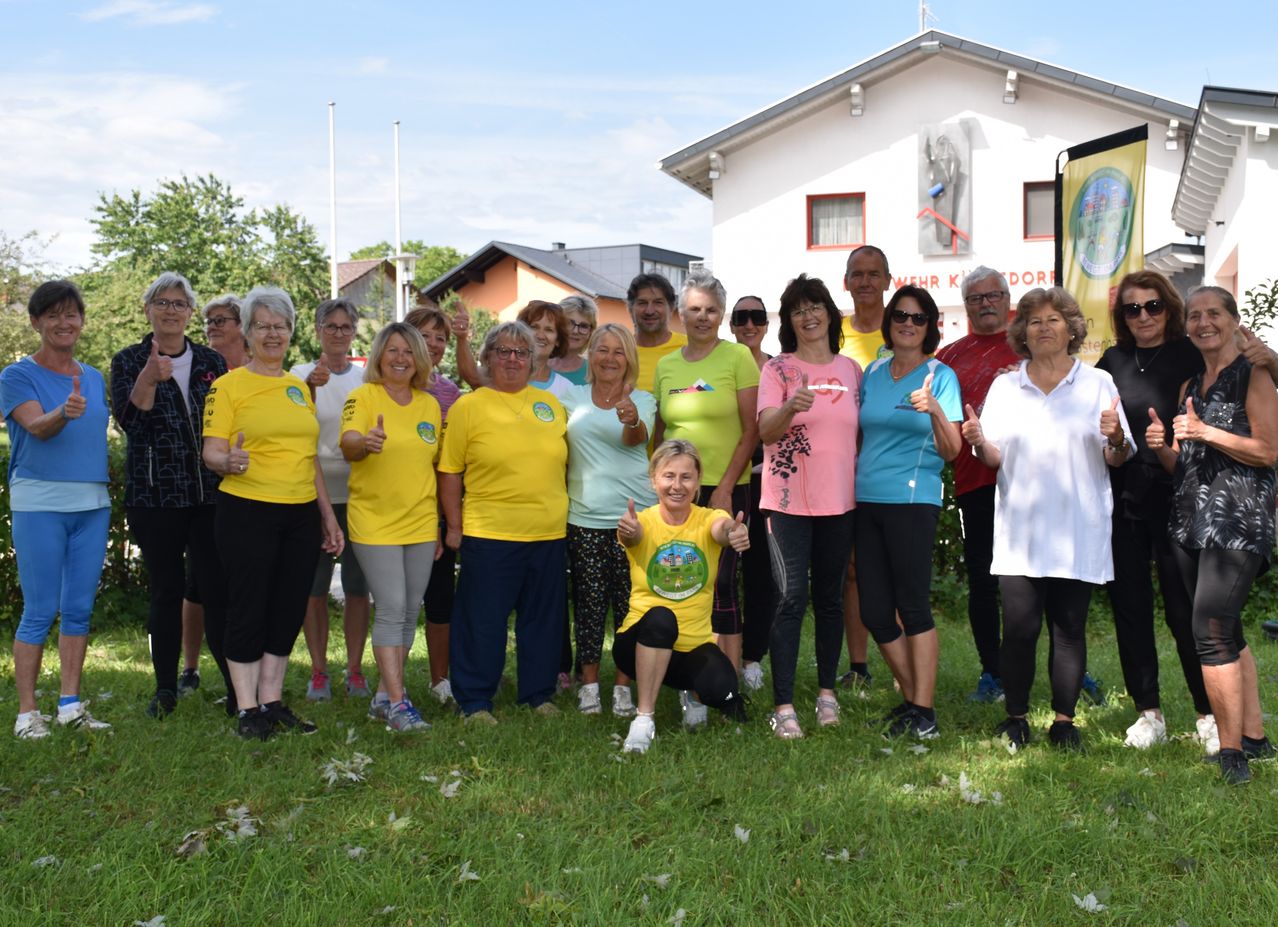 Eine Gruppe von Menschen in gelben, rosa und blauen T-Shirts posiert für ein Foto vor einem Gebäude mit einem Banner an der Seite.