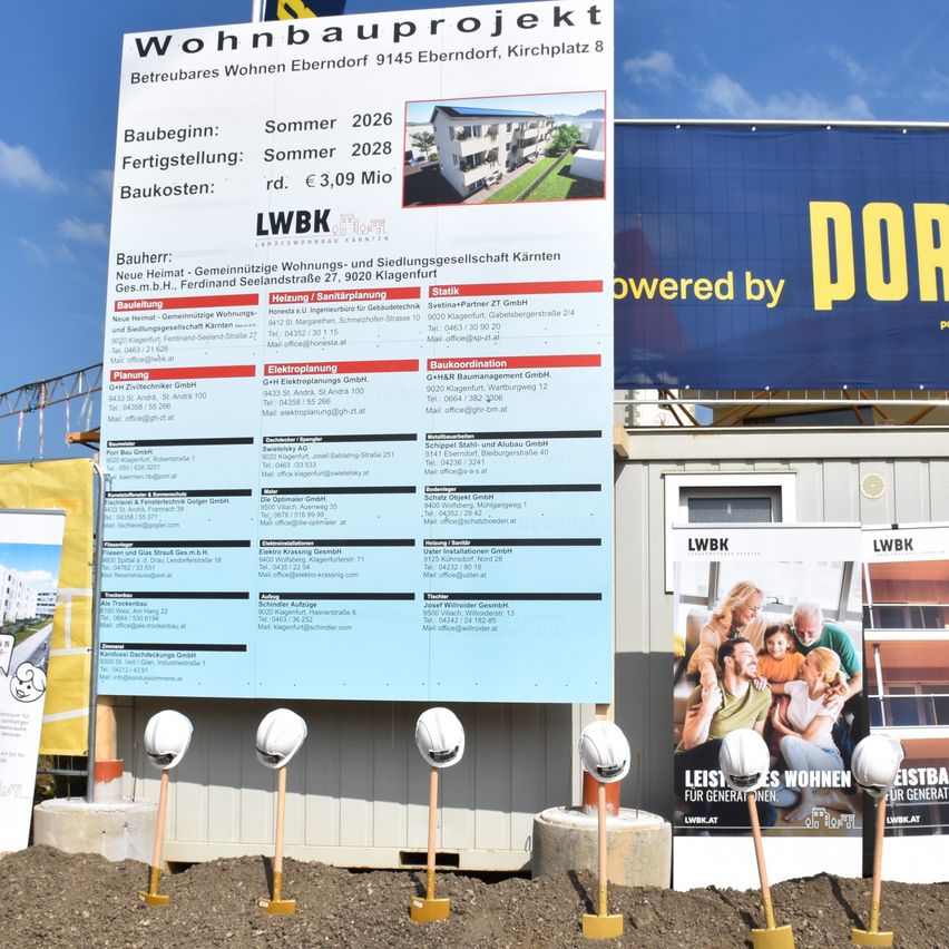 A large signboard displays information about a housing project in Eberndorf, including the start and completion dates, costs, and contact details for various contractors and services.