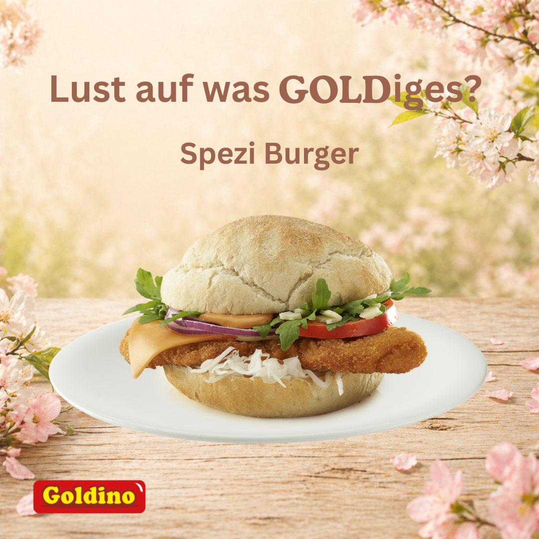 Ein Goldino Burger mit Käse, Tomate, Zwiebeln und Salat auf einem weißen Teller. Rosa Blumen und ein unscharfer Hintergrund.