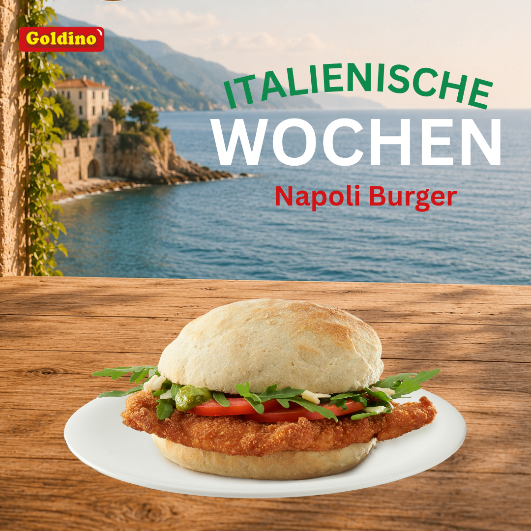 A Napoli Burger sandwich is displayed on a white plate on a wooden table with a scenic view of the sea and mountains in the background. The sandwich is topped with lettuce, tomato, and pesto sauce. The image is part of an advertisement for Goldino Italianische Wochen.
