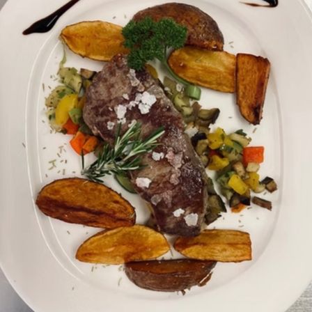 Ein weißer Teller mit Steak, Kartoffeln und Gemüse. Der Teller hat einen schwarzen Schokoladen-Drizzle.