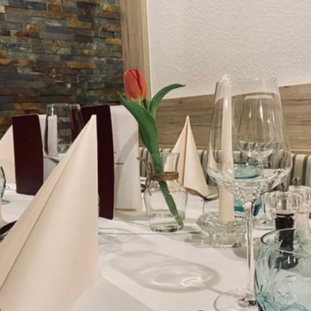 Ein gut gedeckter Tisch in einem Restaurant mit einer roten Tulpe in einer Vase, Weingläsern, Besteck und Servietten.