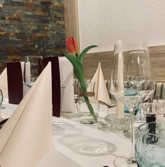 A well-set table in a restaurant with a red tulip in a vase, wine glasses, cutlery, and napkins.