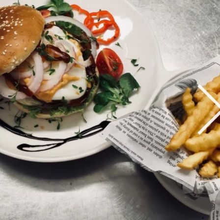Ein Teller mit einem Burger, der mit roten Zwiebeln, Tomaten und einem grünen Blatt auf einem silbernen Tisch belegt ist.
