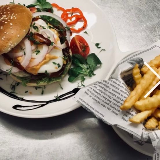 A plate with a burger topped with red onions, tomatoes, and a green leaf on a silver table.