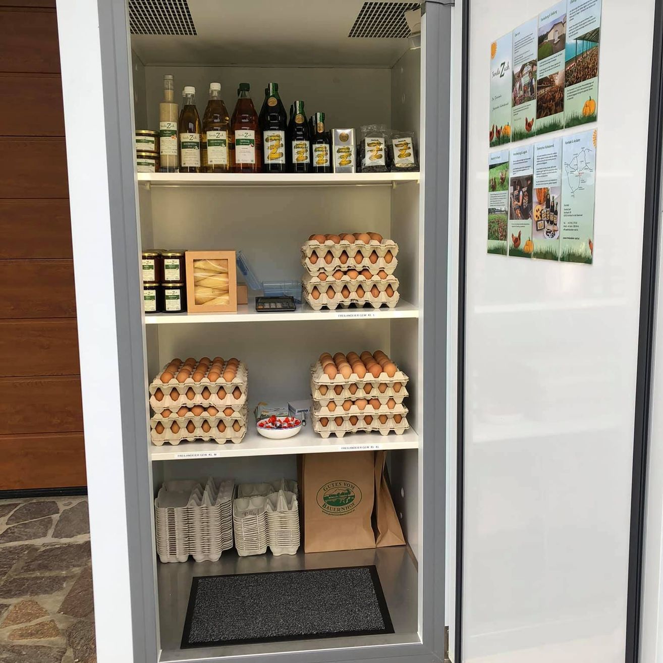 Ein Schrank voller Eier, Gläser und Flaschen. Die Eier sind ordentlich in Kartons angeordnet. Der Schrank ist offen und unten befindet sich ein Fußabtreter.