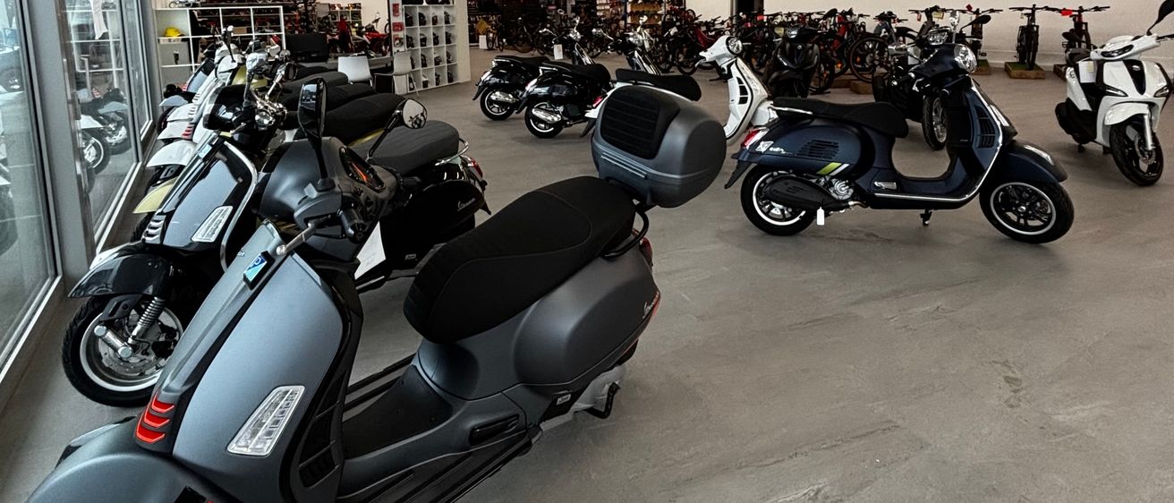 Ein Showroom mit mehreren Rollern, die in einer Reihe geparkt sind und von Deckenleuchten beleuchtet werden.