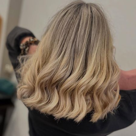 Eine Frau mit langen, welligen blonden Haaren in lockeren Wellen, die ein schwarzes Oberteil trägt.