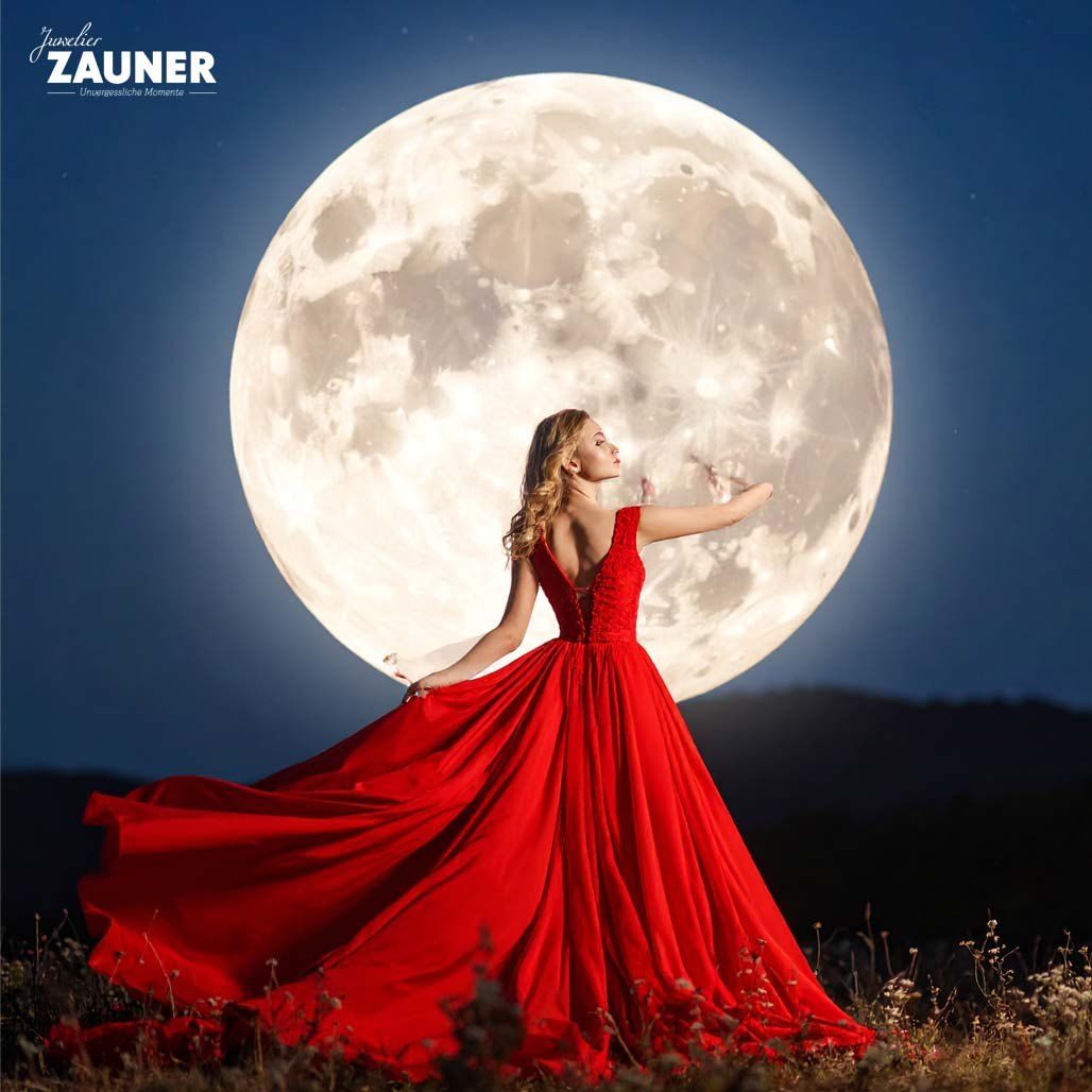 Eine Frau in einem roten Kleid posiert bei Nacht unter einem Vollmond, mit Bergen im Hintergrund.