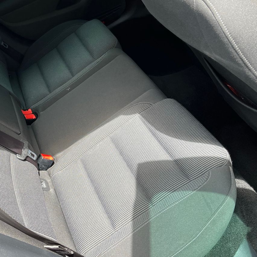 Autoinnenraum mit zwei grauen Ledersitzen, sichtbaren Nähten, Sicherheitsgurt-Schnallen und Sonnenlicht, das Schatten auf die Sitze wirft.