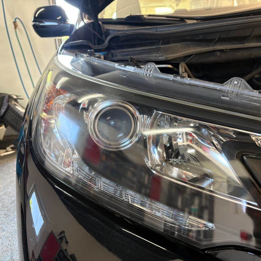 A close-up of a car's headlight with the hood open, showing the headlight assembly and grille.