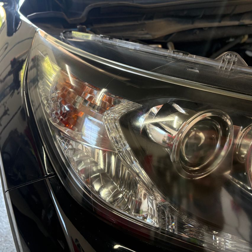 A close-up view of a car's headlight with the hood open, showing the headlight assembly and its reflective surface.