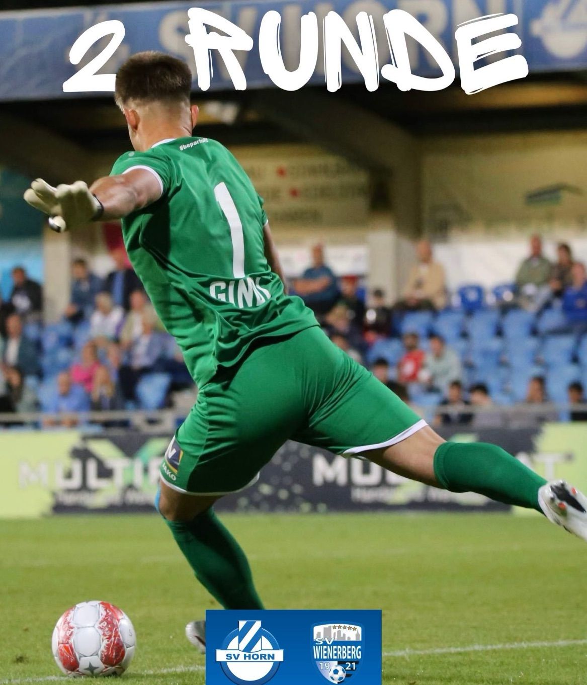 Ein Fußballspieler in einem grünen Trikot mit der Nummer 1 taucht ab, um einen Ball in einem Stadion mit Zuschauern zu blockieren.