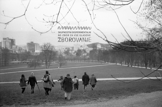 Eine Gruppe von Menschen geht durch einen Park mit Gebäuden und Bäumen im Hintergrund.